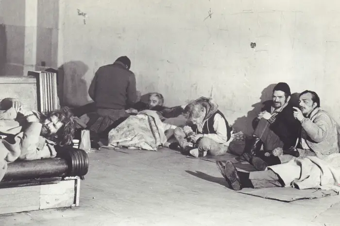 A black and white photograph of a group of homeless men sitting in Grand Central Station in 1985.